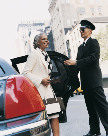 A chauffeur holds the door of a black sedan for a passenger.