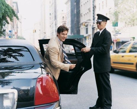 A chauffeur opens a sedan door for a business passenger.