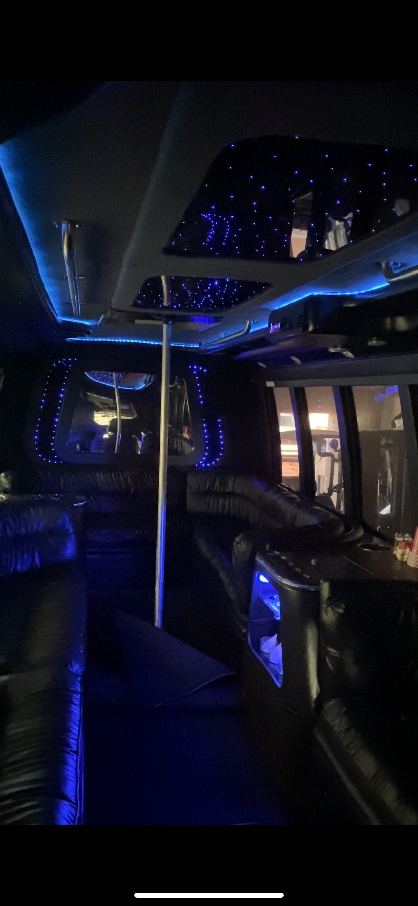 Inside a party bus with wraparound lounge seating and blue star-lighting.
